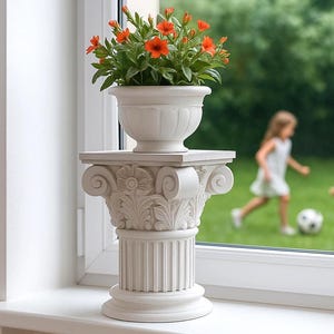 Puede incluir: Un macetero blanco ornamentado, sobre una base de columna con detalles florales, con flores naranjas vibrantes. El macetero está en un alféizar. Niños jugando al fútbol en el fondo, visibles a través de la ventana.