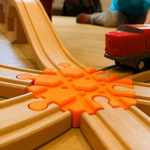 May include: Wooden toy train set with a red train car on a wooden track. The track includes a bridge and an orange connector piece. The train car has black wheels and the number 1800 on the side. The track is made of light brown wood.