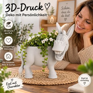 May include: A light gray 3D-printed PLA donkey-shaped planter featuring a wide, toothy grin and long ears. The hollow body holds a lush green plant with small white flowers. The planter is displayed on a round, woven, natural-colored mat.