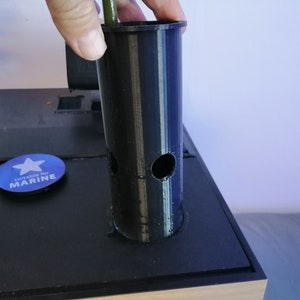 Puede incluir: Una maceta de plástico negra con dos agujeros en el lateral. La maceta está siendo sostenida por una mano y está sentada sobre una superficie negra. El texto "Suitable for MARINE" es visible en una pegatina azul.