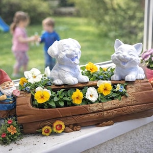 May include: A decorative window box planter with a smiling white puppy and cat figurine, surrounded by yellow and white pansies. A garden gnome and other decorative items are also present. The planter is made of brown wood.