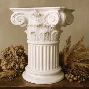 Puede incluir: Una columna blanca de estilo clásico con intrincadas tallas y un fuste acanalado. La columna se coloca sobre una superficie de madera y está rodeada de arreglos florales secos. El capitel de la columna presenta volutas enrolladas y ornamentación detallada.