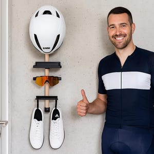 May include: A wall-mounted bicycle helmet and gear organizer. The white helmet is above a pair of orange-tinted cycling glasses and a pair of white athletic shoes. The organizer is made of wood and black metal. A man in a cycling jersey gives a thumbs up.