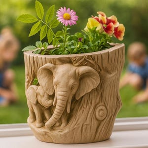 May include: A beige planter featuring an elephant design, filled with colourful flowers. The planter has a textured, tree-trunk effect with a large elephant and a baby elephant carved into the front. The flowers include pink and yellow blooms.