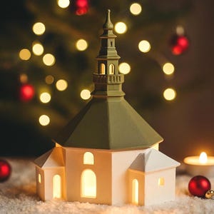 以下が含まれることがあります： 白と緑の教会型のクリスマスオーナメント。窓が光っています。オーナメントは雪の表面に置かれ、赤いオーナメントとろうそくが背景にあります。背景には、ぼやけたクリスマスツリーとボケライトがあります。