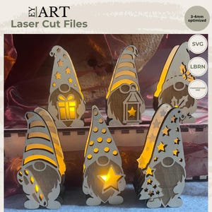 Peut inclure: Six figurines de gnomes en bois découpées au laser avec des motifs ajourés incluant des étoiles, des rayures, un cadeau, une lanterne et un sapin. Les figurines sont éclairées par l'arrière d'une lumière jaune chaude. Texte : EY ART, Laser Cut Files, 3-4mm optimized, SVG, LBRN, Commercial use.