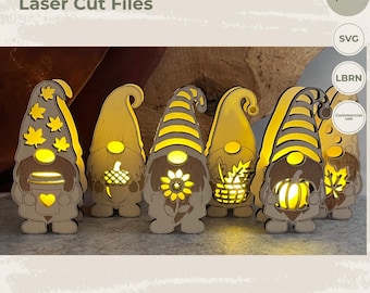 May include: A set of six light-colored wooden gnome cutouts featuring laser-cut designs including maple leaves, an acorn, a sunflower, a basket of leaves, a pumpkin, and a single leaf. The text EY ART Laser Cut Files is visible at the top.