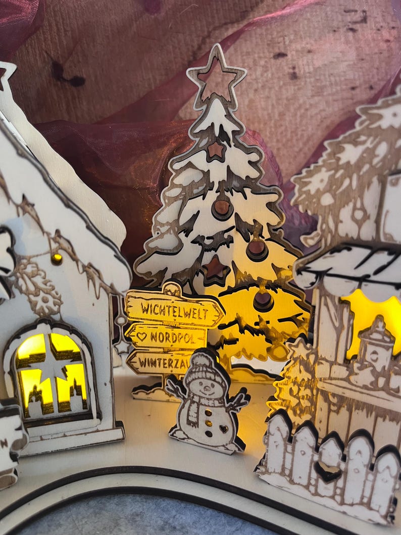 K&ouml;nnte beinhalten: Ein dekoratives Weihnachtsdorf-Set aus Holz mit beleuchteten wei&szlig;en H&auml;usern, einem stilisierten Baum und einem Schneemann. Ein Wegweiser zeigt die Aufschrift WICHTELWELT, NORDPOL und WINTERZAUBER. Die Teile haben dunkle Kanten und warmes Licht.