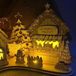 K&ouml;nnte beinhalten: Eine beleuchtete h&ouml;lzerne Weihnachtsmarktszene mit einem Stand mit der Aufschrift WEIHNACHTS MARKT, einem geschm&uuml;ckten Baum, einem Schneemann und einem Wegweiser mit den W&ouml;rtern WICHTELWELT, NORDPOL und WINTERZAUBER. Das Display leuchtet warmgelb.