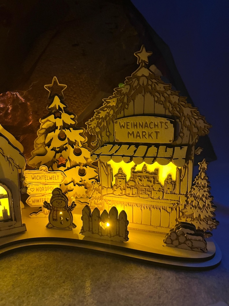 K&ouml;nnte beinhalten: Eine beleuchtete h&ouml;lzerne Weihnachtsmarktszene mit einem Stand mit der Aufschrift WEIHNACHTS MARKT, einem geschm&uuml;ckten Baum, einem Schneemann und einem Wegweiser mit den W&ouml;rtern WICHTELWELT, NORDPOL und WINTERZAUBER. Das Display leuchtet warmgelb.