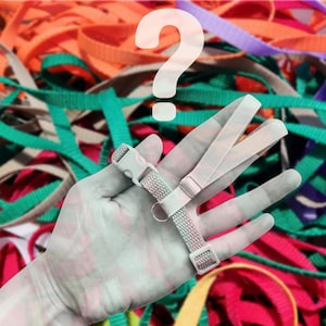 May include: A white plastic adjustable lanyard with a black plastic buckle. The lanyard is held in a hand against a background of colorful fabric straps.