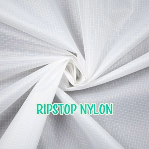 May include: White ripstop nylon fabric with a grid pattern. The fabric is folded and twisted, showing its texture. The text "RIPSTOP NYLON" is printed in green on the fabric.