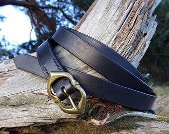 Pode incluir: Um cinto de couro preto com uma fivela de metal dourado. A fivela tem a forma de um coração com um design decorativo. O cinto está enrolado em torno de um pedaço de madeira.