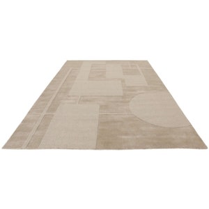 Può includere: Tappeto rettangolare beige con un motivo geometrico. Il tappeto presenta una serie di rettangoli, quadrati e un semicerchio in varie tonalità di beige. Il design è moderno e minimalista, adatto a soggiorni o camere da letto.