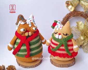 May include: Two crocheted gingerbread cat ornaments, one with a red scarf and the other with a green scarf. Both cats are wearing striped sweaters and have white frosting on their heads. The cats are sitting on wooden bases.