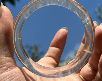 May include: A clear quartz bangle bracelet with a smooth, polished finish. The bracelet is made of natural quartz crystal and has a delicate, translucent appearance.