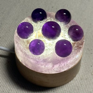 Peut inclure: Une lampe en cristal d'améthyste violette avec une base en bois et sept sphères d'améthyste sur le dessus.