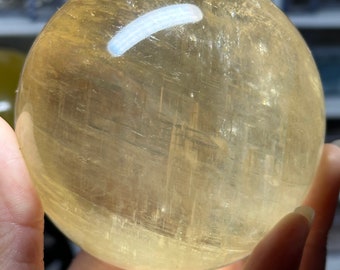 May include: A large, smooth, yellow citrine sphere with visible internal striations. The sphere is being held in a hand.