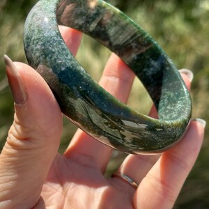 Op de afbeelding: Een groene en bruine jade armband. Het gladde, gepolijste oppervlak van de armband vertoont een mix van groene en bruine tinten. De tekst "NO.1" is zichtbaar in de afbeelding.