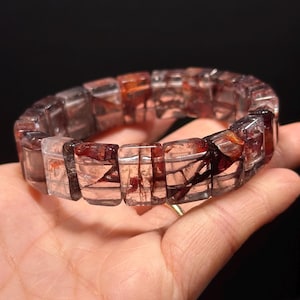 Può includere: Un braccialetto di cristallo rosso e trasparente con perline rettangolari. Le perline hanno un motivo unico a marmo.