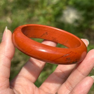 Pode incluir: Um bracelete de jaspe vermelho. O bracelete é liso e polido, com um visual natural e terroso.