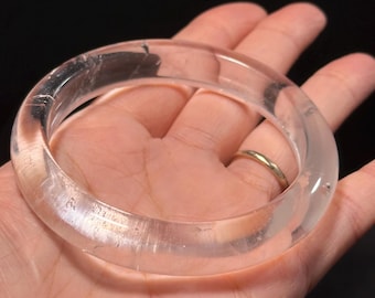 May include: A clear quartz bangle bracelet. The bracelet is smooth and polished, with a slightly rounded shape.