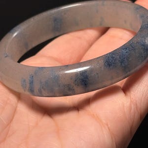 Puede incluir: Un brazalete de color gris claro con motas azules. El brazalete es liso y pulido.