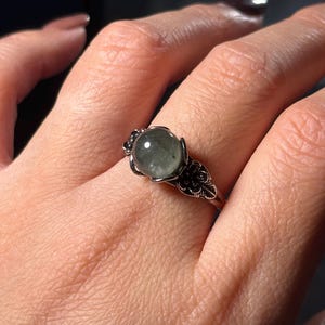 Op de afbeelding: Een zilveren ring met een ronde, groene edelsteen in een bloemmotief.