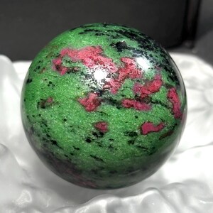 Op de afbeelding: Een groene en roze bol van gepolijst zultanite edelsteen. De bol heeft een glad, gepolijst oppervlak en is een levendige groene kleur met roze en zwarte insluitsels.