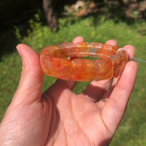 Könnte beinhalten: Ein Karneol-Armband in Orange- und Rottönen. Das Armband besteht aus glatten, polierten Steinen und hat eine quadratische Form.