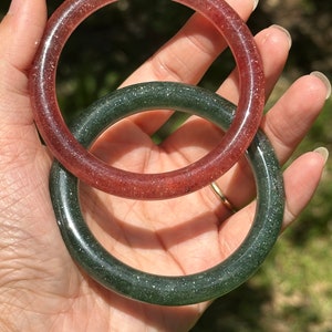 Op de afbeelding: Twee resin armbanden, een is donkergroen met glitter en de andere is lichtroze met glitter.