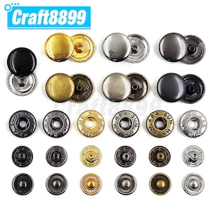 Puede incluir: Surtido de botones a presión de metal en varios colores y acabados, incluyendo negro, plata, oro y latón. Algunos botones tienen un diseño decorativo, mientras que otros son lisos. Los botones están dispuestos en filas sobre un fondo blanco.