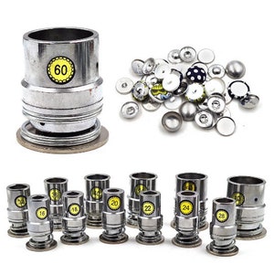 May include: A set of ten silver metal snap button pliers with yellow labels indicating different sizes, including 16, 18, 20, 22, 24, 28, 36, 40, and 60. The pliers are arranged in two rows on a white surface.