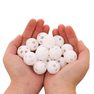 Puede incluir: Un puñado de bolas de plástico blancas con pequeños agujeros por todas partes. Las bolas están en las manos de una persona.
