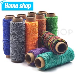Puede incluir: Un conjunto de coloridas bobinas de hilo, incluyendo azul, gris, naranja, marrón, verde, morado y turquesa. Las bobinas están dispuestas verticalmente y de lado. El texto "Hamo shop" está en un cuadro azul en la esquina superior izquierda.