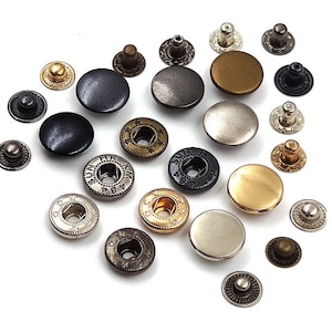 Puede incluir: Surtido de cierres de botón metálicos en varios colores y acabados, incluyendo negro, plateado, dorado y bronce. Algunos cierres tienen detalles decorativos y texto grabado. Estos cierres se utilizan para ropa y accesorios.