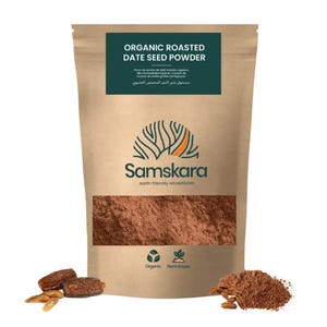 Pode incluir: Uma bolsa bege de pó de semente de tâmara torrada orgânica com um rótulo verde escuro com o texto Organic Roasted Date Seed Powder e Samskara. A embalagem exibe um logótipo de árvore, ícones orgânicos e vegetais, e tâmaras soltas.