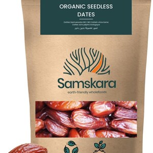 Op de afbeelding: Een bruine stazak met biologische ontpitte dadels met een donkergroen label met de tekst Organic Seedless Dates, Samskara en earth-friendly wholefoods. De zak heeft een venster met bruine dadels en twee losse dadels aan de voorzijde.