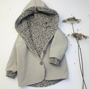 Könnte beinhalten: Eine hellgraue Kapuzenjacke mit Leopardenmuster-Futter. Die Jacke hat einen einzigen Knopfverschluss und ist aus einem weichen, wasserabweisenden Material gefertigt.