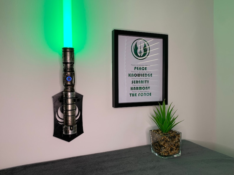 "3D printed Star Wars lightsaber wall mount display with Jedi Code art print. Perfect for showcasing your lightsaber hilt! Ideal decor for fans & collectors. Adds Jedi ambiance to any room. Great gift for Star Wars enthusiasts!"