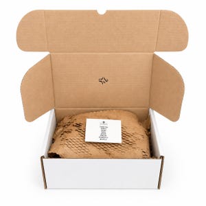 K&ouml;nnte beinhalten: Ein offener Versandkarton aus Pappe mit wei&szlig;er Au&szlig;enseite und brauner Innenseite. Im Inneren umgibt braunes Wabenpapier als F&uuml;llmaterial eine kleine wei&szlig;e Karte, die mit folgendem Text bedruckt ist: THANK YOU, TANK U, DANKE, MERCI, GRAZIE, GRACIAS, DZIĘKUJĘ CI, ありがとう.