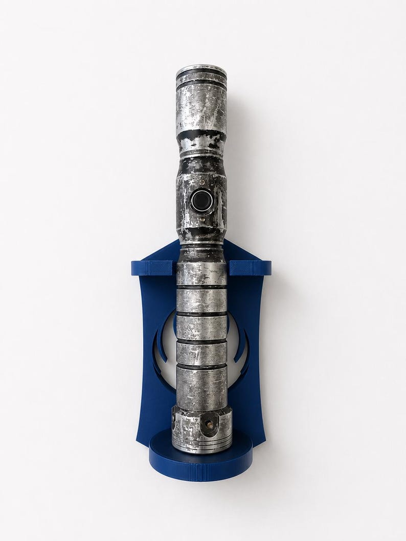 K&ouml;nnte beinhalten: Ein metallisch silberner und schwarzer, verwitterter Lichtschwertgriff, der vertikal an einer dunkelblauen Wandhalterung aus Kunststoff befestigt ist. Der Griff hat ein zylindrisches Design mit horizontalen Rillen und einem runden Schalter.