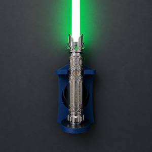 K&ouml;nnte beinhalten: Ein silberfarbener Lichtschwertgriff mit komplexen Metallgravuren und einer leuchtenden gr&uuml;nen Klinge, vertikal montiert an einer dunkelblauen Wandhalterung mit einem kreisf&ouml;rmigen Jedi-Orden-Symbol in der Mitte des Griffs.