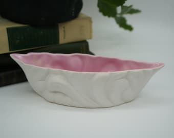May include: A white ceramic bowl with a pink interior and a textured, leaf-like design. The bowl is shaped like a boat or a canoe.