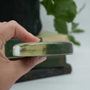 May include: A clear glass paperweight with a slightly rounded edge. The paperweight is resting on a stack of books.