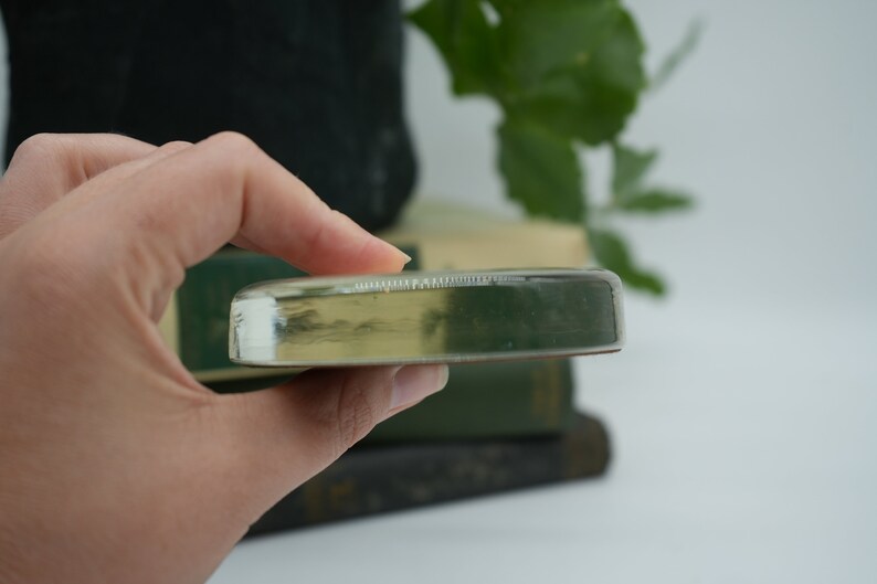 May include: A clear glass paperweight with a slightly rounded edge. The paperweight is resting on a stack of books.