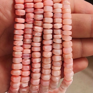 May include: Strands of pink opal beads. The beads are small, rectangular, and have a slightly faceted appearance. The color varies from a pale, almost translucent pink to a deeper, more opaque shade. The beads are strung together, creating a delicate and elegant look.