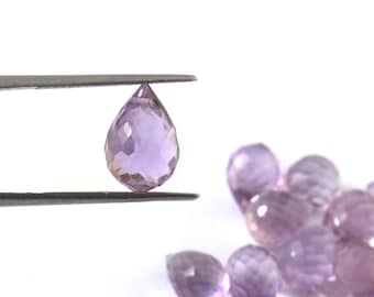 May include: A faceted, teardrop-shaped amethyst gemstone is held by tweezers, showcasing its light purple color and intricate cut. Several similar gemstones are scattered in the background against a white backdrop, highlighting the gem's clarity and shape.