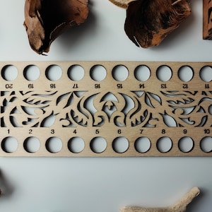 Peut inclure: Un bol à laine en bois avec 20 trous numérotés pour ranger la laine. Le bol a un motif floral décoratif.