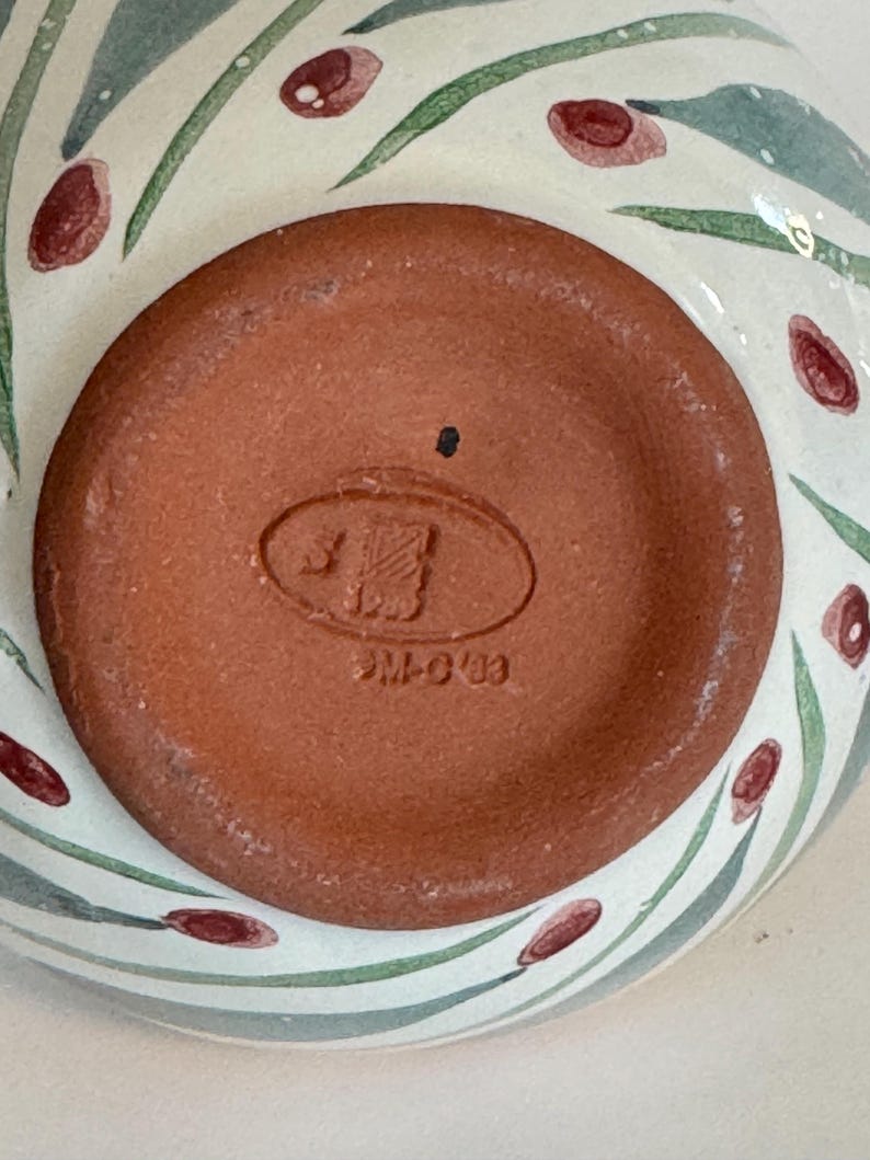 K&ouml;nnte beinhalten: Nahaufnahme des Bodens einer Keramikschale. Der Schalenboden ist rotbraun mit einem gepr&auml;gten Stempel. Die Au&szlig;enseite der Schale hat einen wei&szlig;en Hintergrund mit gr&uuml;n und rot bemalten floralen Designs.